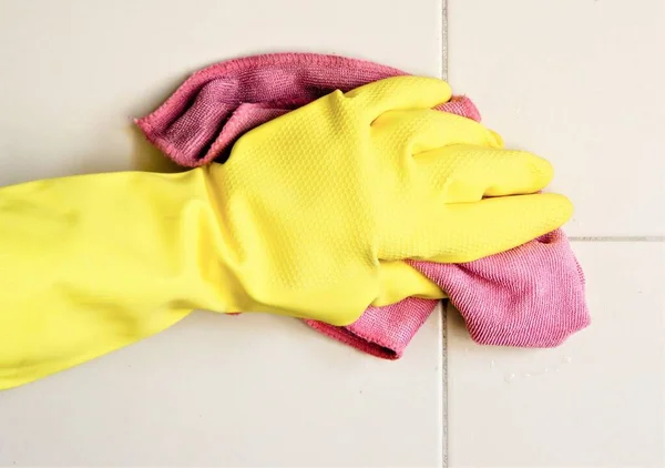 Hand in protective glove cleaning tiles with rag. Cleaning house