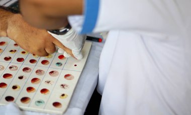 Laboratuvar teknisyeni hastanedeki kan grubunu öğrenmek için hastadan kan örneği alıyor.