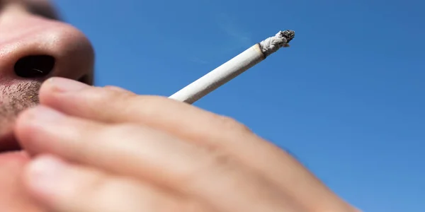 Sigaretta in mano contro il cielo blu — Foto Stock