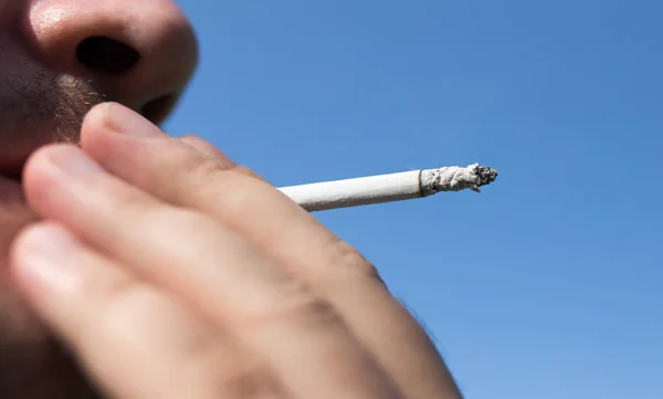 Sigaretta in mano contro il cielo blu — Foto Stock