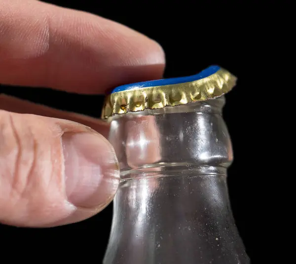 Glazen fles met een dop in zijn hand op een zwarte achtergrond — Stockfoto