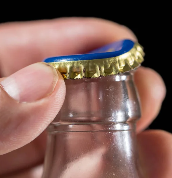 Glass bottle with a cap in his hand on a black background — Stock Photo, Image