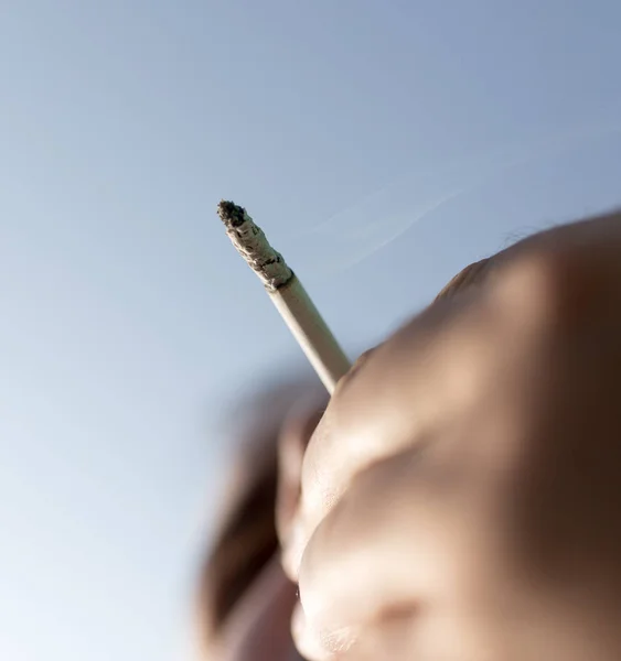 Cigarro na mão contra o céu azul — Fotografia de Stock