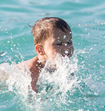 Çocuk su parkında su sıçratarak yüzüyor.