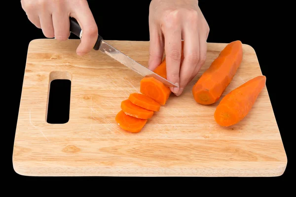 Bucătar taie morcovi pe o placă pe un fundal negru — Fotografie, imagine de stoc