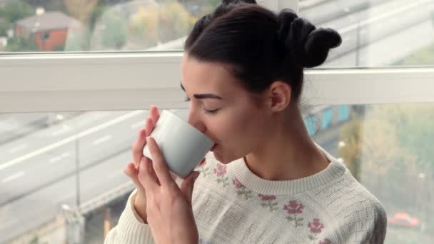 迷人的年轻女子坐在靠近窗口，喝咖啡 — 图库视频影像