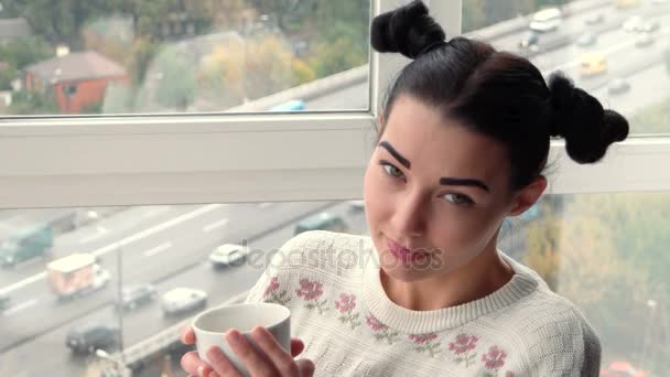 Charmante jonge vrouw zitten in de buurt van venster en drinken koffie — Stockvideo