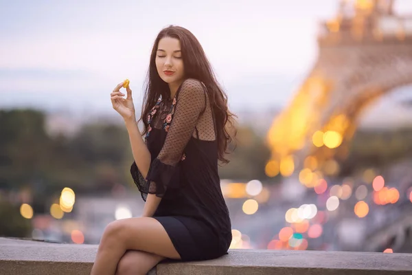 Paris woman smiling eating the french pastry macaron in Paris against Eiffel tower.