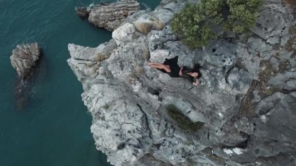 Vista aérea da jovem mulher no penhasco de rocha contra o mar — Vídeo de Stock