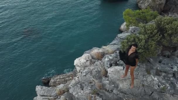 Vista aérea da jovem mulher no penhasco de rocha contra o mar — Vídeo de Stock