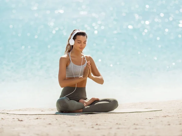 Femme dans la pose de méditation de yoga avec écouteurs sur la plage — Photo