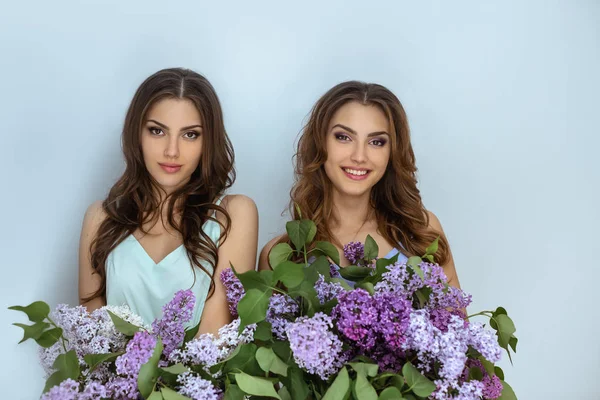 Studio photo portrait de mode de deux jumelles femmes avec un bouquet de fleurs de printemps — Photo