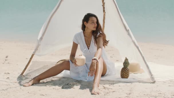 Mulher bebendo suco de coco enquanto relaxa na praia — Vídeo de Stock