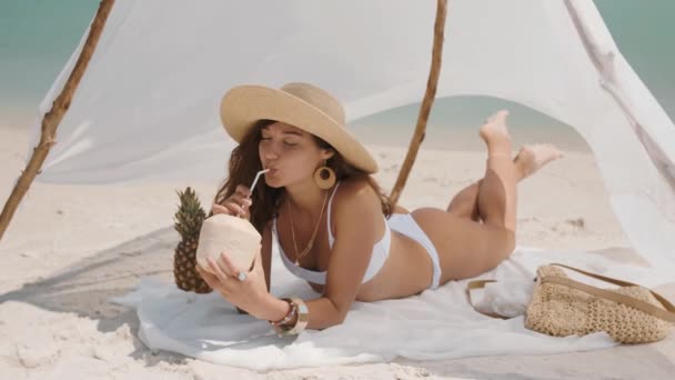 Egy nő kókuszlevet iszik, miközben a strandon pihen. — Stock videók