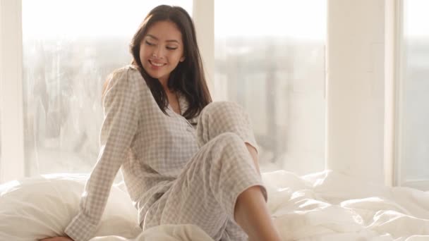 Азиатка, сидящая на кровати дома — стоковое видео