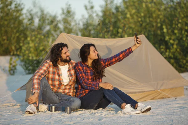 Happy Couple With a Smartphone in the Camp Near the Tent Outdoors — Stock Photo, Image