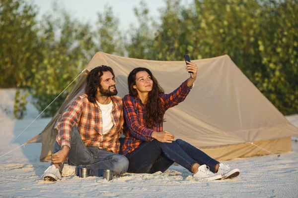Happy Couple With a Smartphone in the Camp Near the Tent Outdoors — Stock Photo, Image