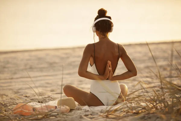 Femme dans la pose de méditation de yoga avec écouteurs sur la plage — Photo