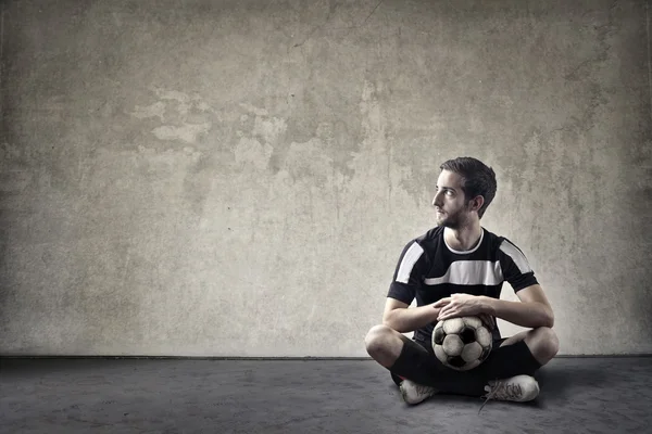Футболист сидит со своим мячом — стоковое фото
