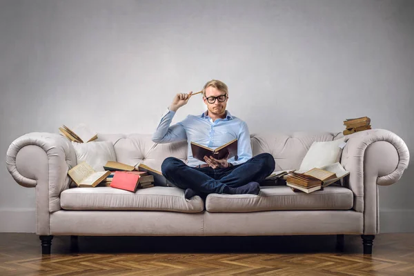 Businessman learning from books on couch — Stock Photo, Image