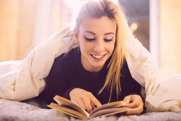 Ξανθιά γυναίκα ανάγνωση κάτω από τις κουβέρτες — Φωτογραφία Αρχείου