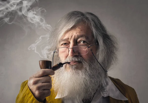 Бородатый старик курит трубку внутри — стоковое фото
