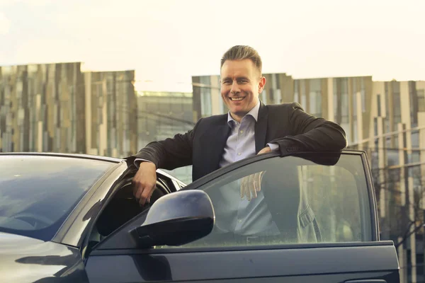 Geschäftsmann lächelt, während er sich an sein Auto lehnt — Stockfoto