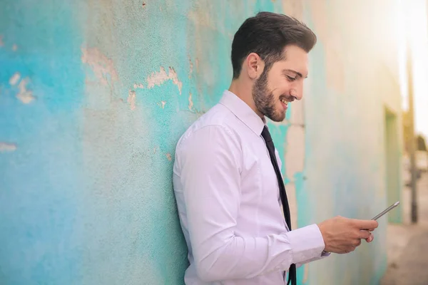 Бородатый бизнесмен с телефоном перед синей стеной — стоковое фото