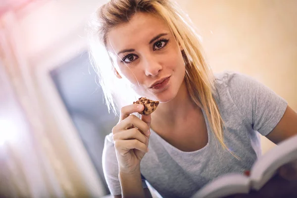 Blond kobieta jedzenie cookie wewnątrz — Zdjęcie stockowe