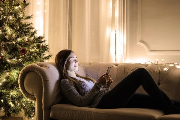 家里有智能手机的女孩与圣诞树 — 图库照片