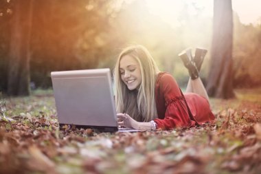 Bir dizüstü bilgisayar kullanırken bir parkta oturan mutlu kız