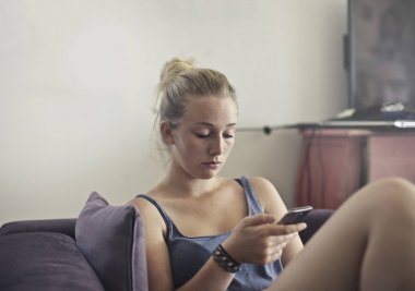 Kanepede oturan bir akıllı telefon kullanan kız