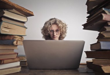 Sarışın öğrenci bir masanın üzerinde bir dizüstü bilgisayar kullanarak 