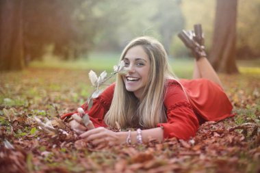 Smiling girl in a red dress lying on a autumn meadow