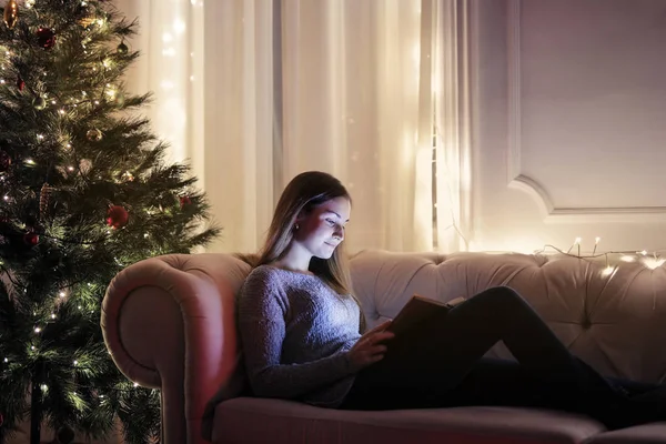 女孩使用膝上型电脑坐在一棵圣诞树附近的沙发上 — 图库照片