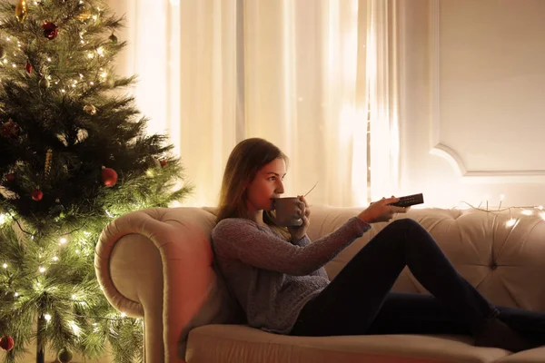 看电视的女孩坐在沙发附近的一棵圣诞树 — 图库照片