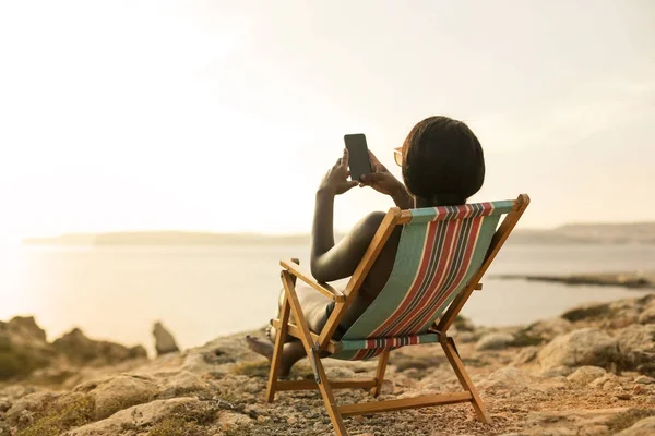 Menina Africana Tomando Banho Sol Beira Mar Enquanto Usa Smartphone — Fotografia de Stock