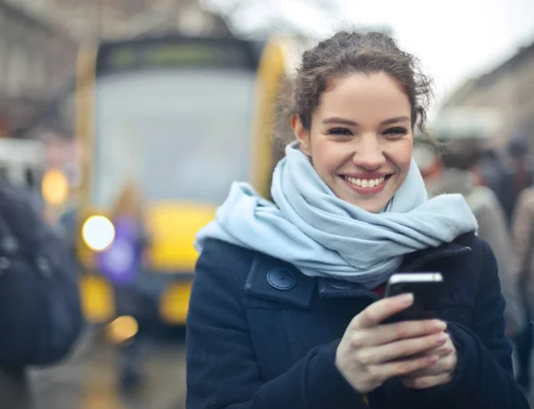 在城市街道上使用智能手机的年轻微笑的妇女 — 图库照片