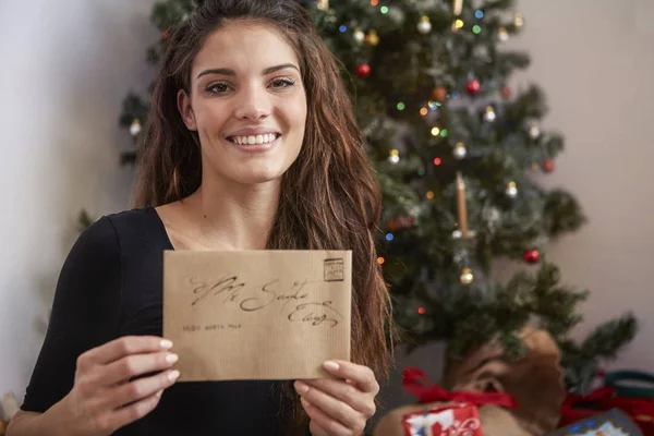 在圣诞树前的一个微笑的女孩的肖像 在她手中的圣诞老人的信 — 图库照片