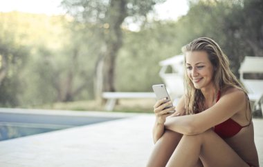 Havuz başı telefon bakarak gülümseyen genç sarışın kadın