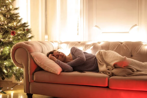 在一棵圣诞树旁边睡在沙发上的女人 — 图库照片