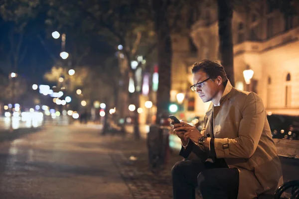 Bir Bankta Oturan Geceleri Sokak Bir Şehirde Cep Telefonunu Kullanarak — Stok fotoğraf