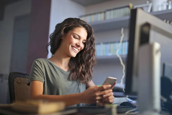 Jeune Femme Caucasienne Assise Sur Bureau Souriant Regardant Son Téléphone — Photo