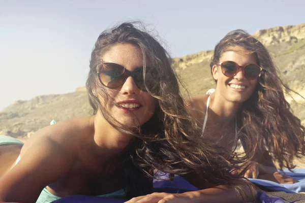 ビーチでの日光浴のサングラスをかけた二人の若い白人女性 — ストック写真