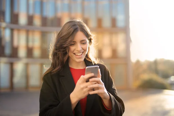 Genç Gülümseyen Beyaz Kadın Telefonunu Bir Kentsel Bağlamda Bakarak — Stok fotoğraf