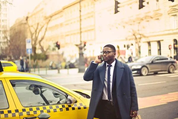 Αφρικανική Επιχειρηματίας Μιλώντας Στο Τηλέφωνο Μπροστά Από Ένα Κίτρινο Ταξί — Φωτογραφία Αρχείου