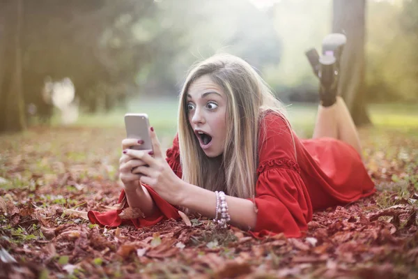 Şaşırmış Genç Bir Kadın Bahçede Akıllı Telefonunu Izliyor — Stok fotoğraf