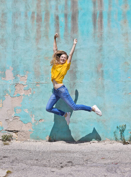 Girl jumping on front of a blue wall
