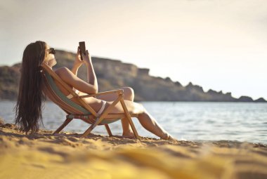 Bir şezlong üzerinde bir akıllı telefon kullanan kız