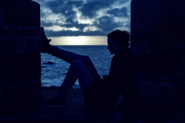 Silhouette of a young woman contemplating sitting on a wall over — Stock Photo, Image